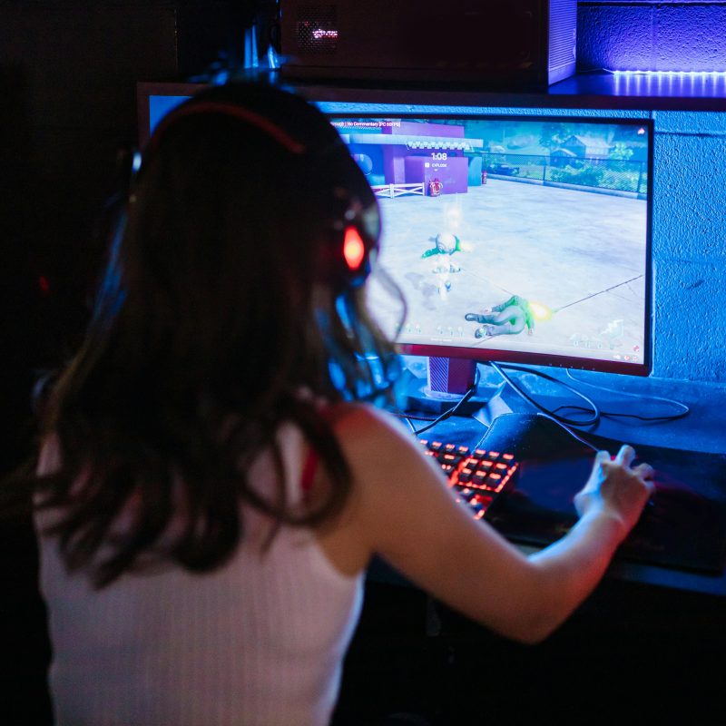 Female gamer focused on playing a competitive online game with RGB keyboard and headphones.