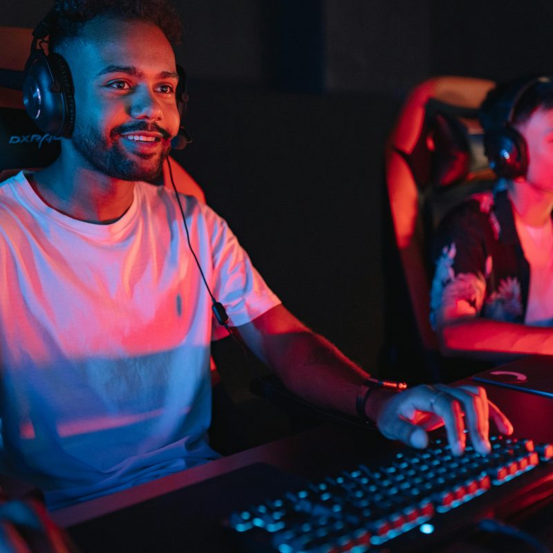 Two male gamers intensely focused during a gaming session in a cybercafe with colorful lighting.